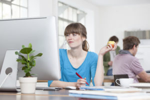 Portrait of young woman eating an apple at her desk in a creative office